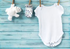 Baby boy clothes and white bear toy on a clothesline on blue wooden background